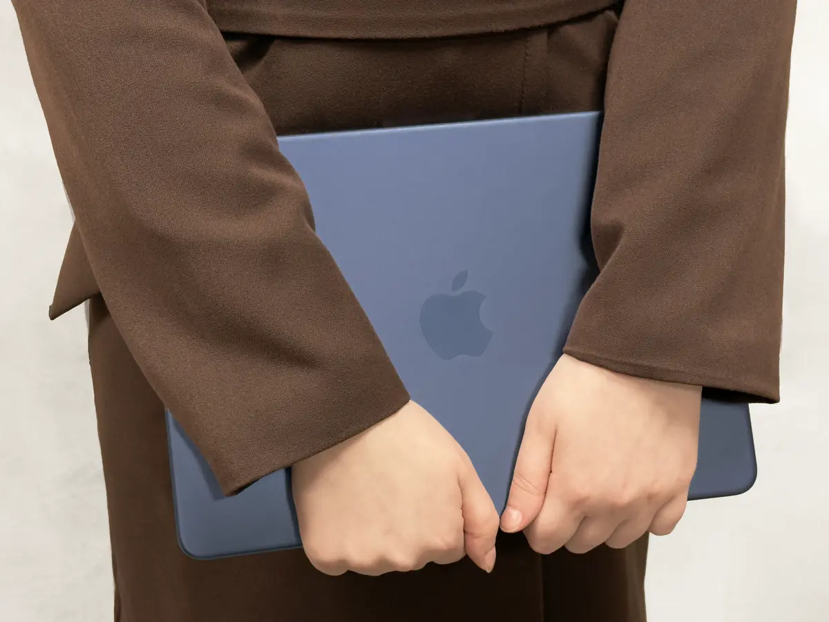 Руки человека держат закрытый синий ноутбук Apple MacBook с логотипом яблока на крышке.