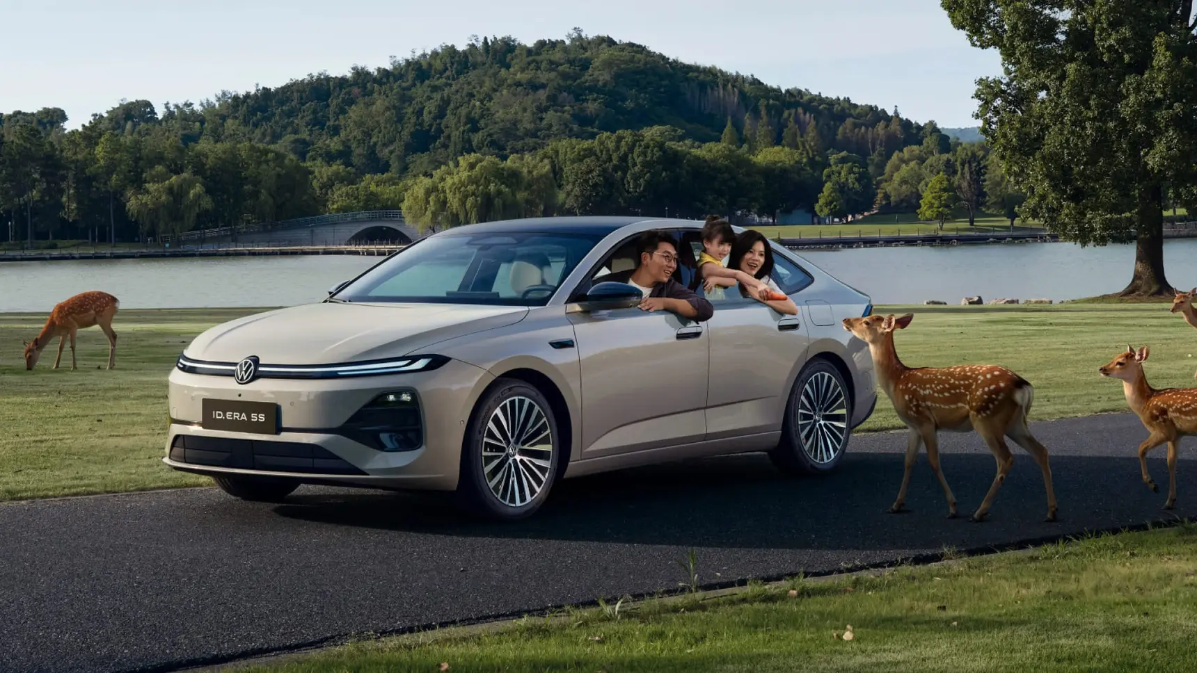 Серебристый седан Volkswagen ID.ERA 5S с семьей, рядом олени на фоне парка.