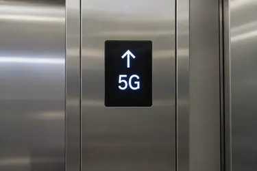 Светящийся дисплей с белой стрелкой вверх и текстом 5G на металлическом фоне.