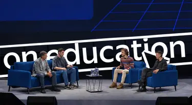 Четыре спикера сидят на синих диванах на сцене конференции oneeducation.
