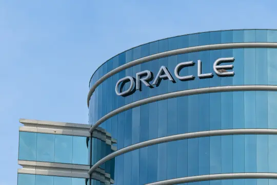 Стеклянное здание с логотипом Oracle и гнездом птицы на фоне неба.