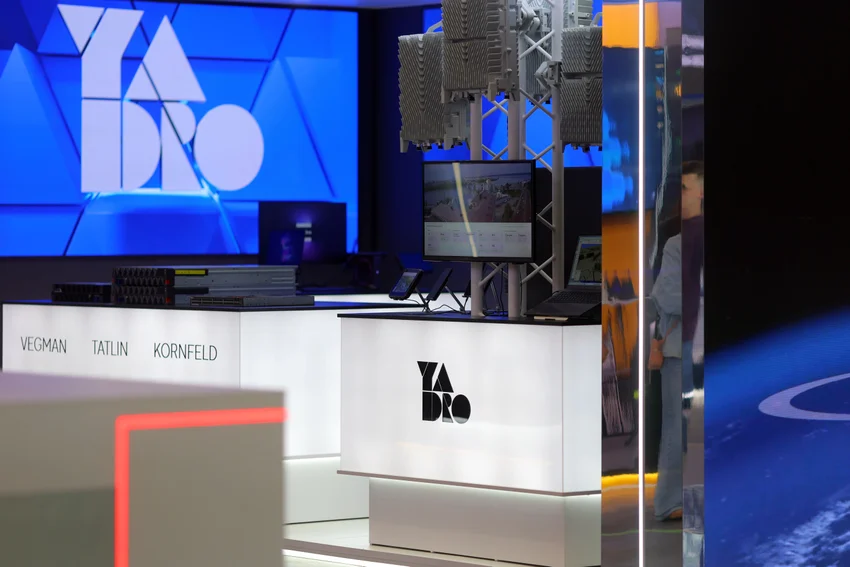 Выставка, стенды компаний, экран с логотипом Yadro, базовые станции Yadro, ноутбук, планшет, люди.