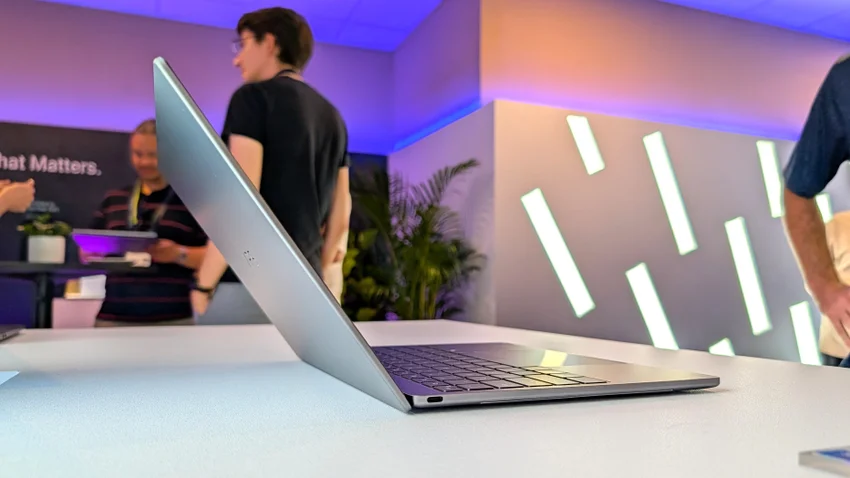 Серебристый ноутбук Dell XPS 13 открыт на столе на фоне выставки с посетителями и подсветкой.