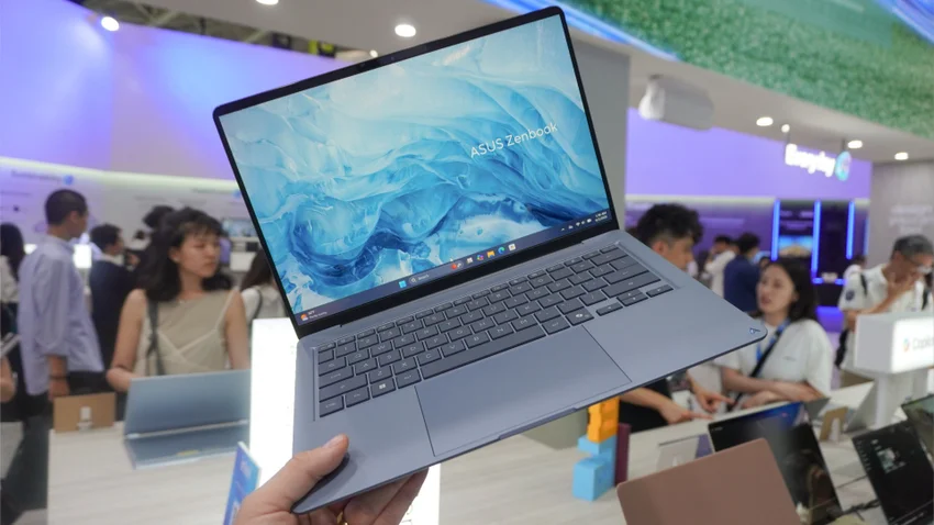 Серо-синий ноутбук ASUS Zenbook с включенным экраном в руке на выставке.
