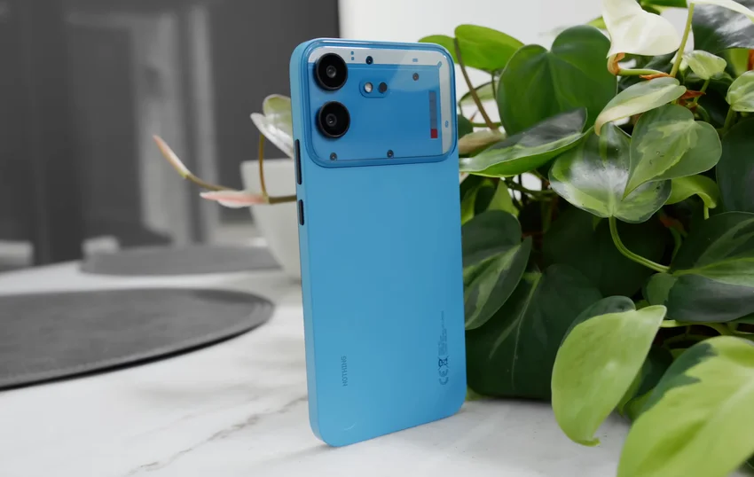 Синий смартфон Nothing Phone (4b) с двумя камерами и полупрозрачной задней панелью у растения.