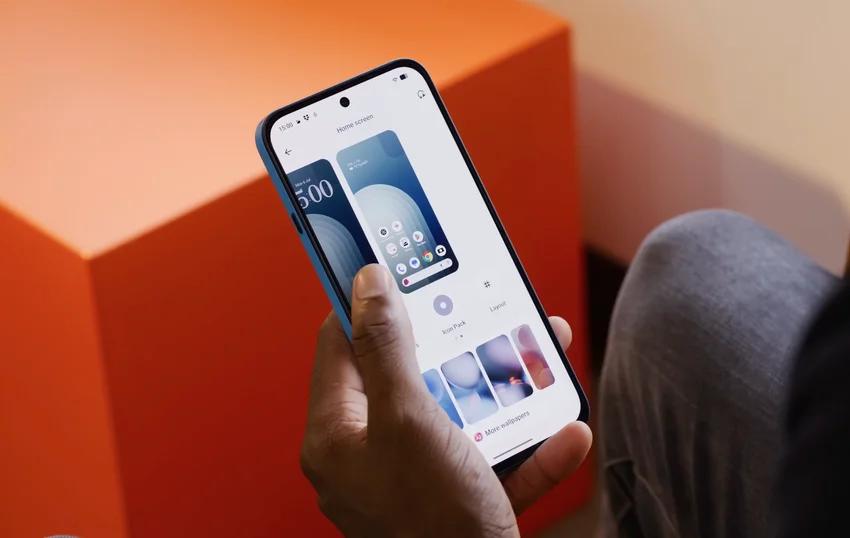 Синий смартфон Nothing Phone (4b) в руке на оранжевом фоне.