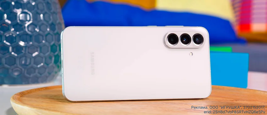 Белый смартфон Samsung с тройной камерой на деревянной поверхности. Рекламная информация.