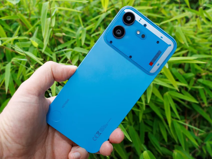 Синий смартфон Nothing Phone (4b) держат в руке на фоне зелени