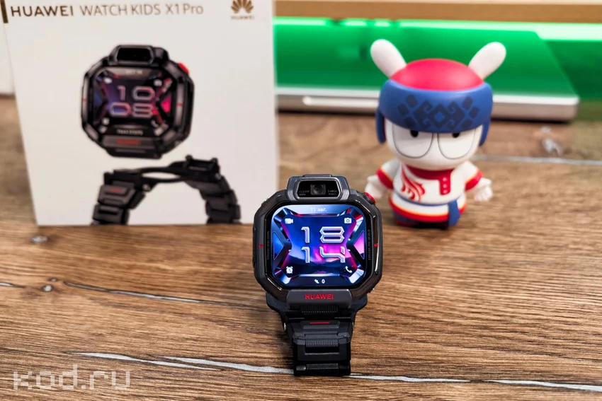 Смарт-часы Huawei Watch Kids X1 Pro с включенным экраном на столе рядом с коробкой и фигуркой.