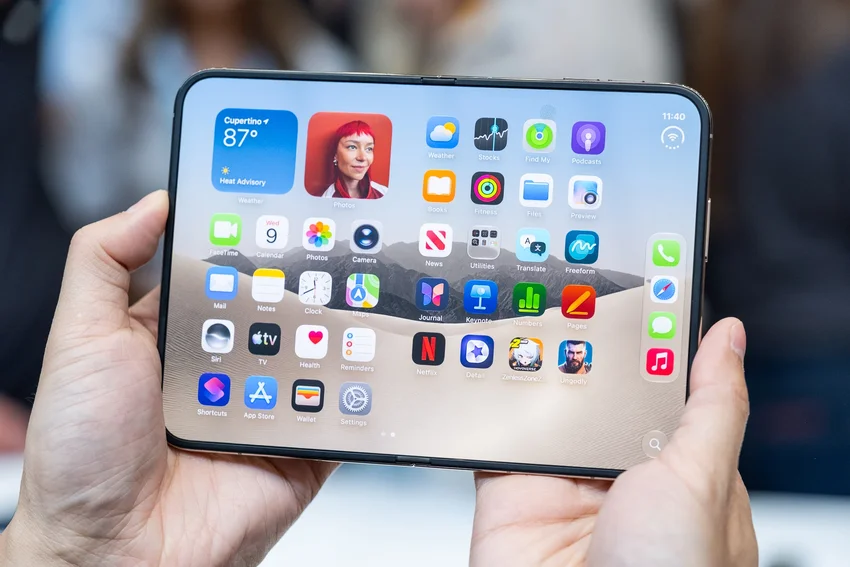 Руки держат раскрытый iPhone Duo с интерфейсом iOS и иконками приложений на экране.