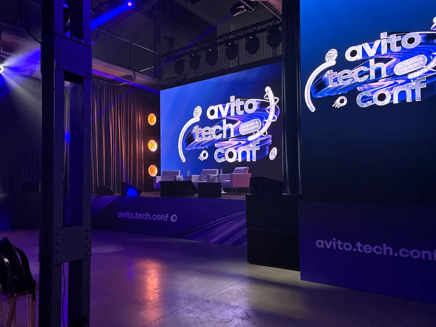 Сцена Avito Tech Conf, экран с логотипом, кресла, синяя подсветка, баннер.